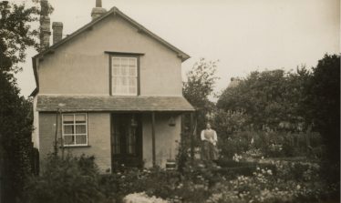 Photograph 8: The Jacklin House stood end on to Chiswick End.  Dolly Jacklin (nee Wing) is standing in the garden.  The edge of the Chiswick Farm Cottages is just visible over the trees. c. 1928 | Bill Wing