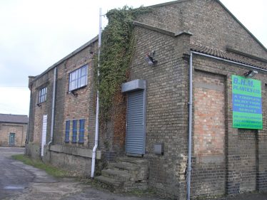 The Warehouse in 2010.  The door and window in the office have been bricked up.  The awning has gone as have the large sliding doors.  The openings have been bricked up.  Note the old stables in the background. | Tim Gane